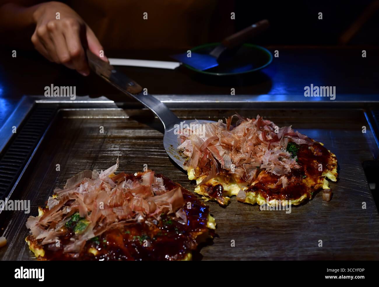 Chef che cucina un okonomiyaki sul piatto di ferro, un popolare cibo locale in Giappone Foto Stock