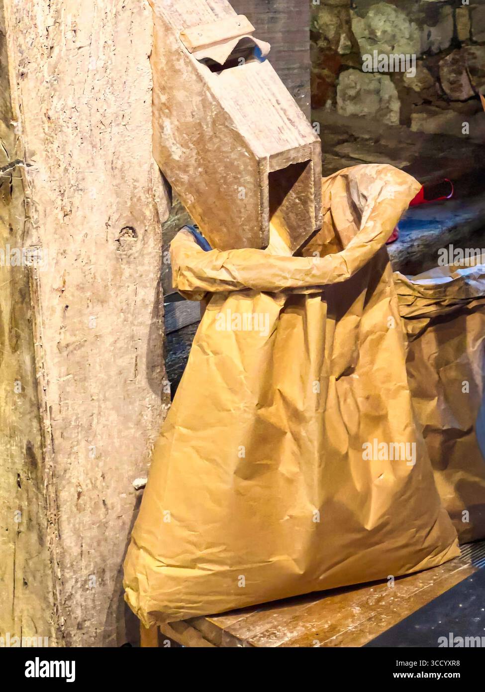 Farina fresca versata da uno scivolo di legno un sacco di carta in un vecchio mulino della città in un ambiente rustico Foto Stock
