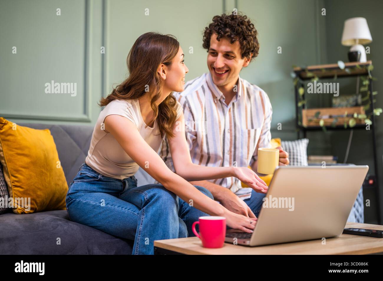 La coppia adulta è seduta sul divano di casa e utilizza un computer portatile. Foto Stock