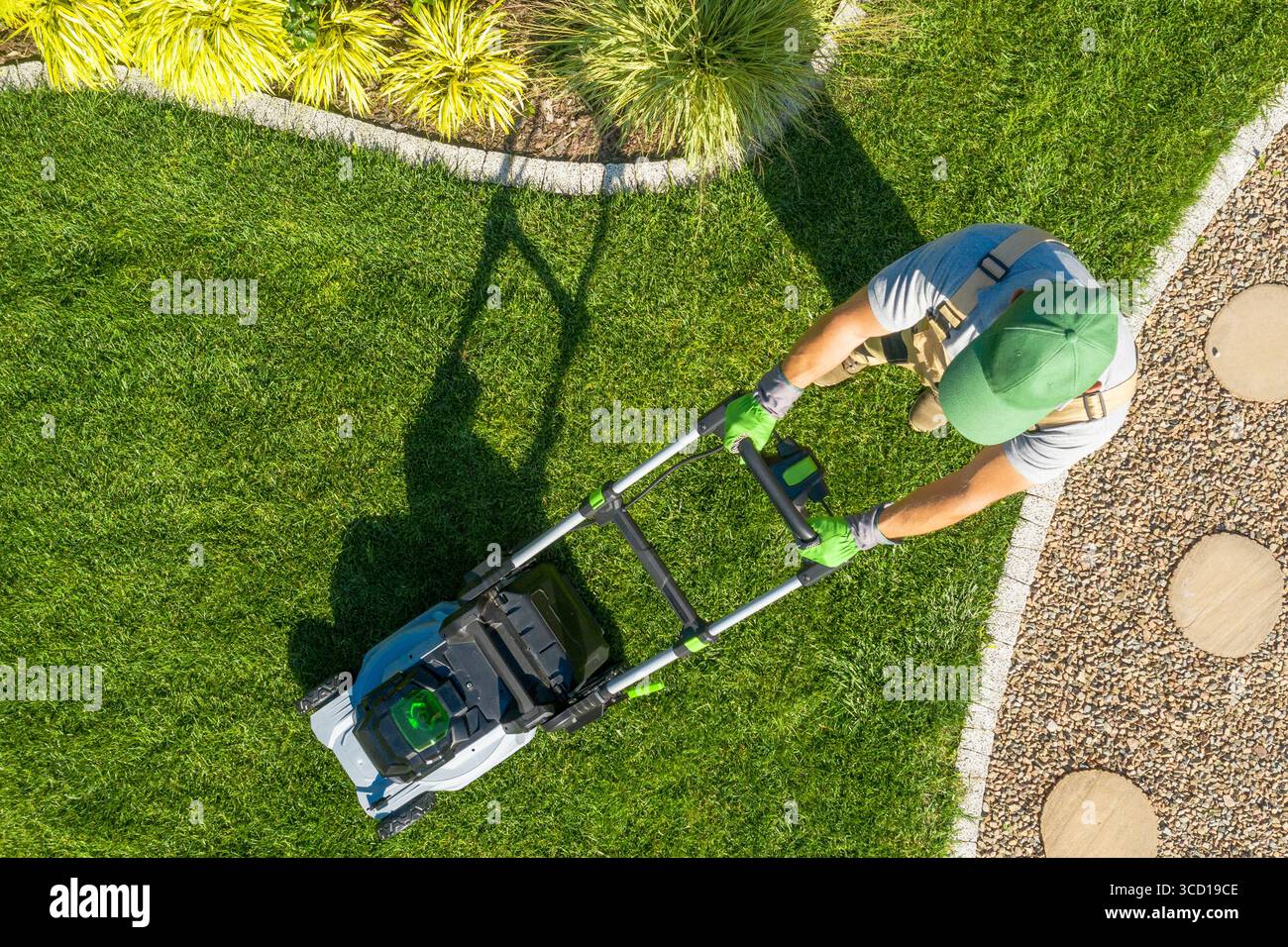 Un professionista della cura del prato rifinisce la lussureggiante erba verde in un giardino ben curato durante il giorno. Le linee dell'erba appena tagliate contrastano con il percorso in pietra. Foto Stock