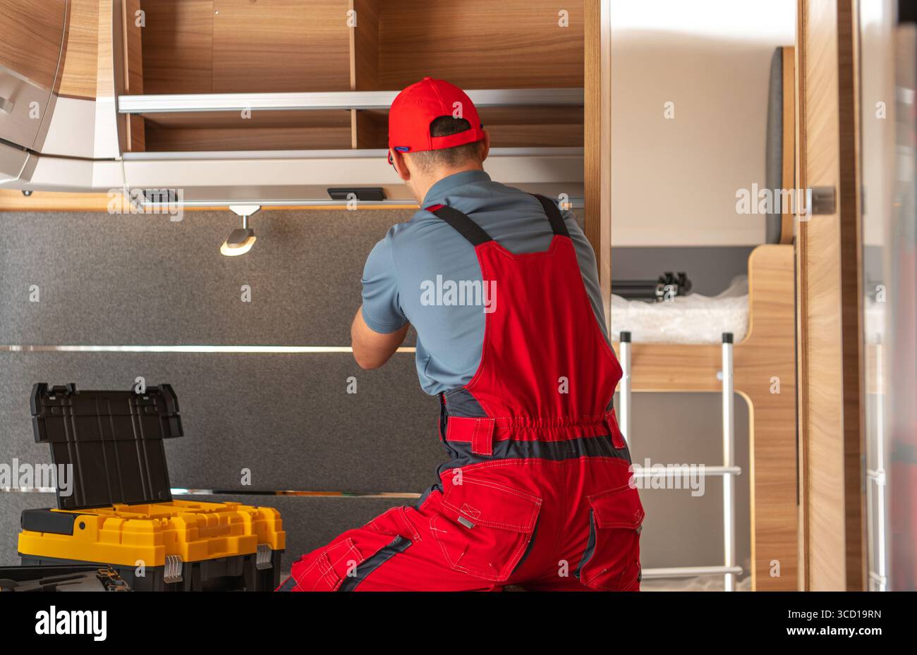 Un lavoratore esperto lavora per organizzare l'area di stoccaggio all'interno di un moderno camper durante il giorno. L'ambiente è elegante e funzionale. Foto Stock