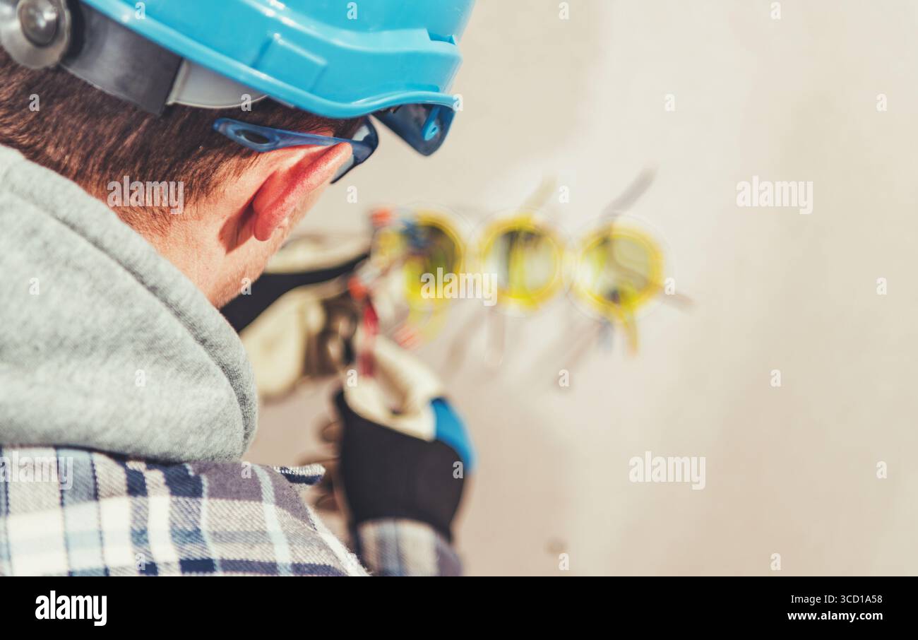 Un elettricista esperto lavora all'installazione di cablaggi elettrici in un edificio in costruzione. L'attenzione ai dettagli è essenziale per la sicurezza e l'efficienza Foto Stock