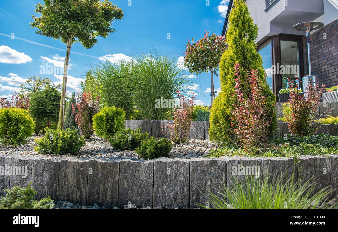 Piante colorate e arbusti ornamentali creano un giardino lussureggiante accanto a una casa moderna in una giornata di sole, mettendo in risalto la bellezza della natura e del design Foto Stock
