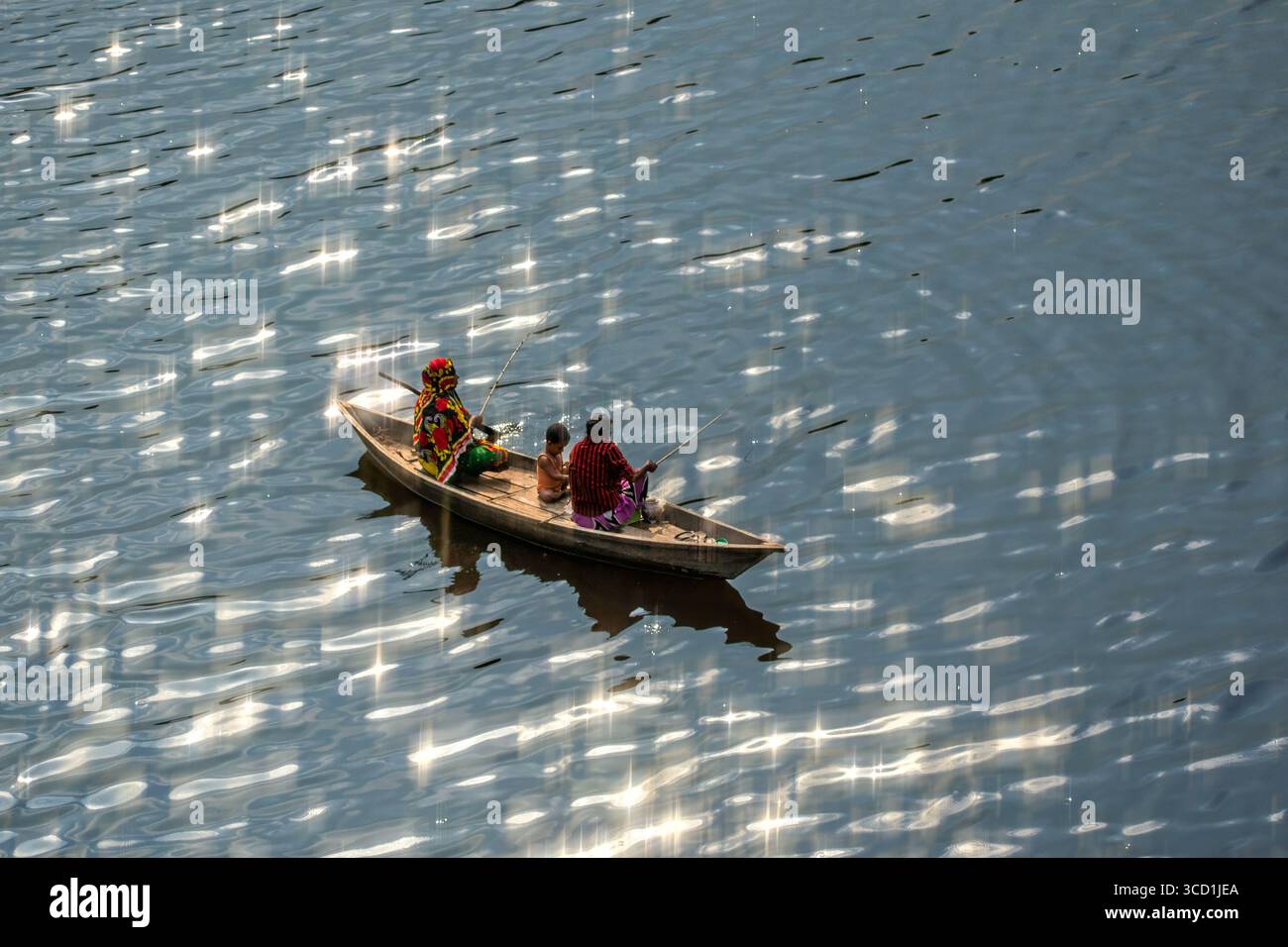 Bogura, Bangladesh - 06 aprile 2018: Veduta di una piccola barca che trasporta tre figure scivola attraverso la superficie scintillante e baciata dal sole di un ampio fiume, che riflette la luce come diamanti sparsi. Foto Stock