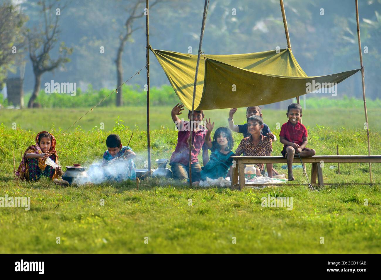 Bogura, Bangladesh - 20 gennaio 2019: Vista dei bambini nascosti sotto una tenda improvvisata, i loro volti si illuminano di risate nel verde del campo. Foto Stock