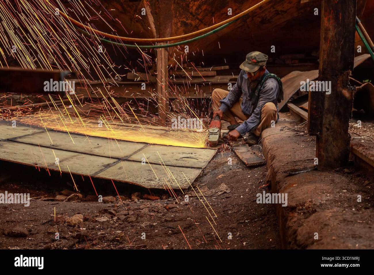 Dhaka, Bangladesh - 25 ottobre 2019: Veduta di un lavoratore in mezzo a una pioggia di scintille mentre macina il metallo in un cantiere navale, l'acciaio grezzo contrastava con il d Foto Stock