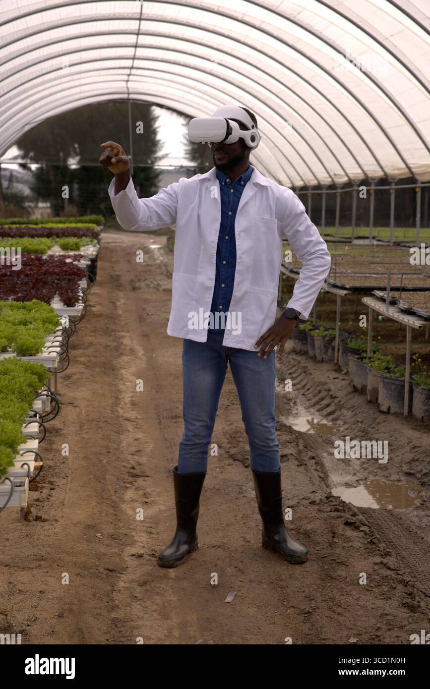 Un ricercatore che indossa il visore VR sta esplorando le vaschette di lattuga idroponiche all'interno di una serra a cerchio Foto Stock