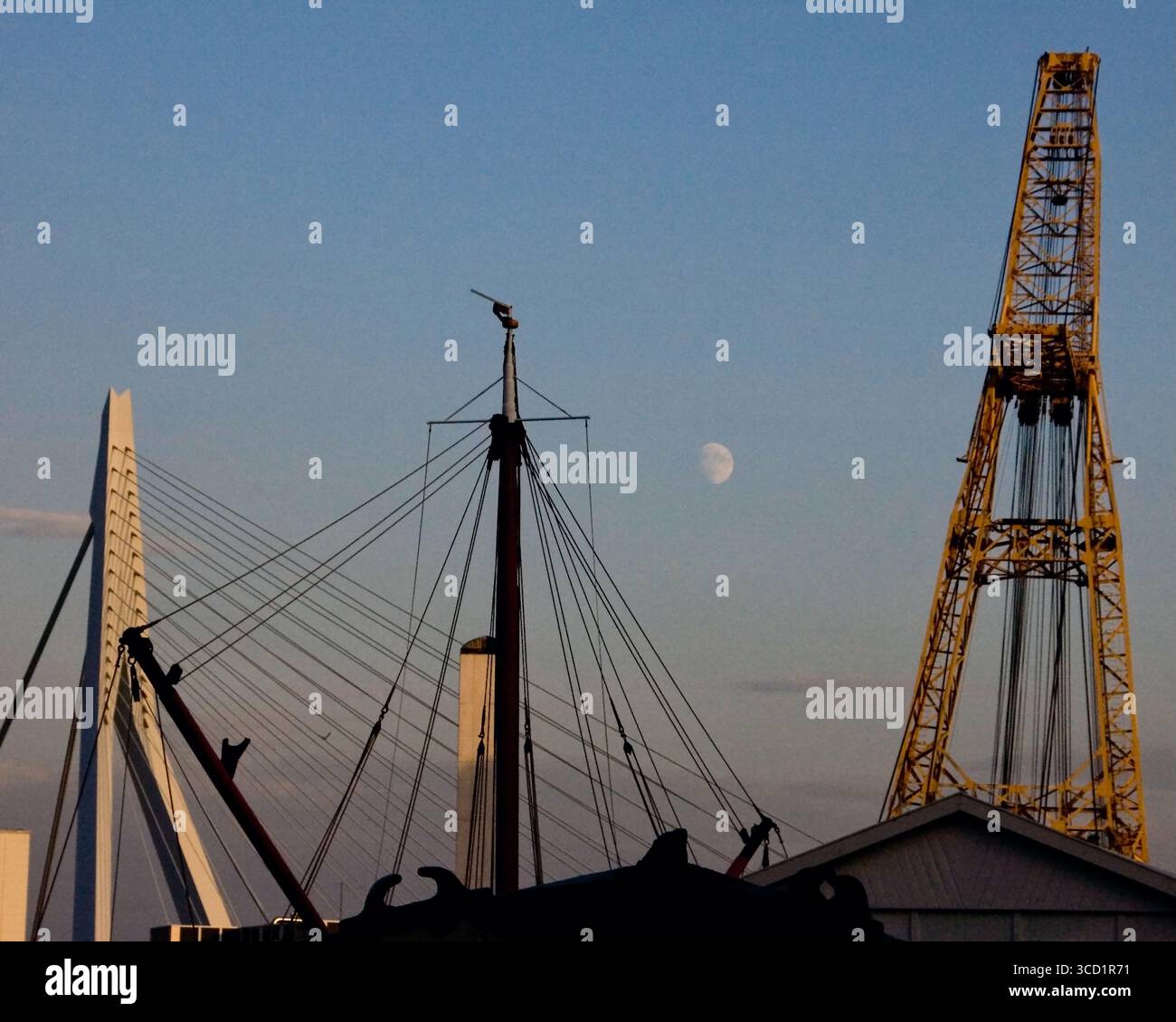 Una vista sagomata dell'albero di una nave, un ponte e una gru contro un cielo blu con la luna visibile. Foto Stock