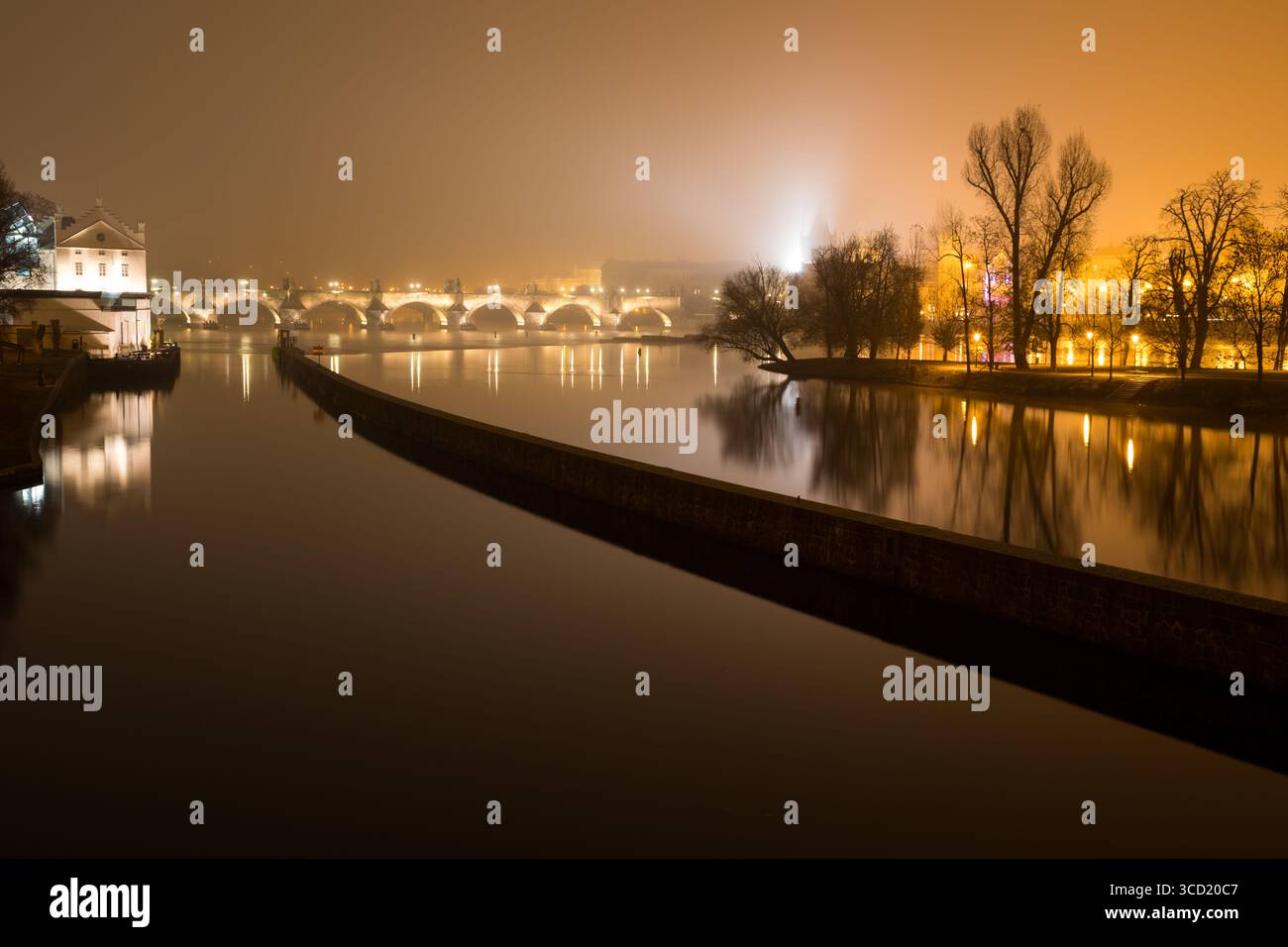 Il Ponte Carlo illuminato a Praga, che brilla di notte, si riflette nelle calme acque del fiume Moldava, le luci della città creano una scena dorata e nebbiosa Foto Stock