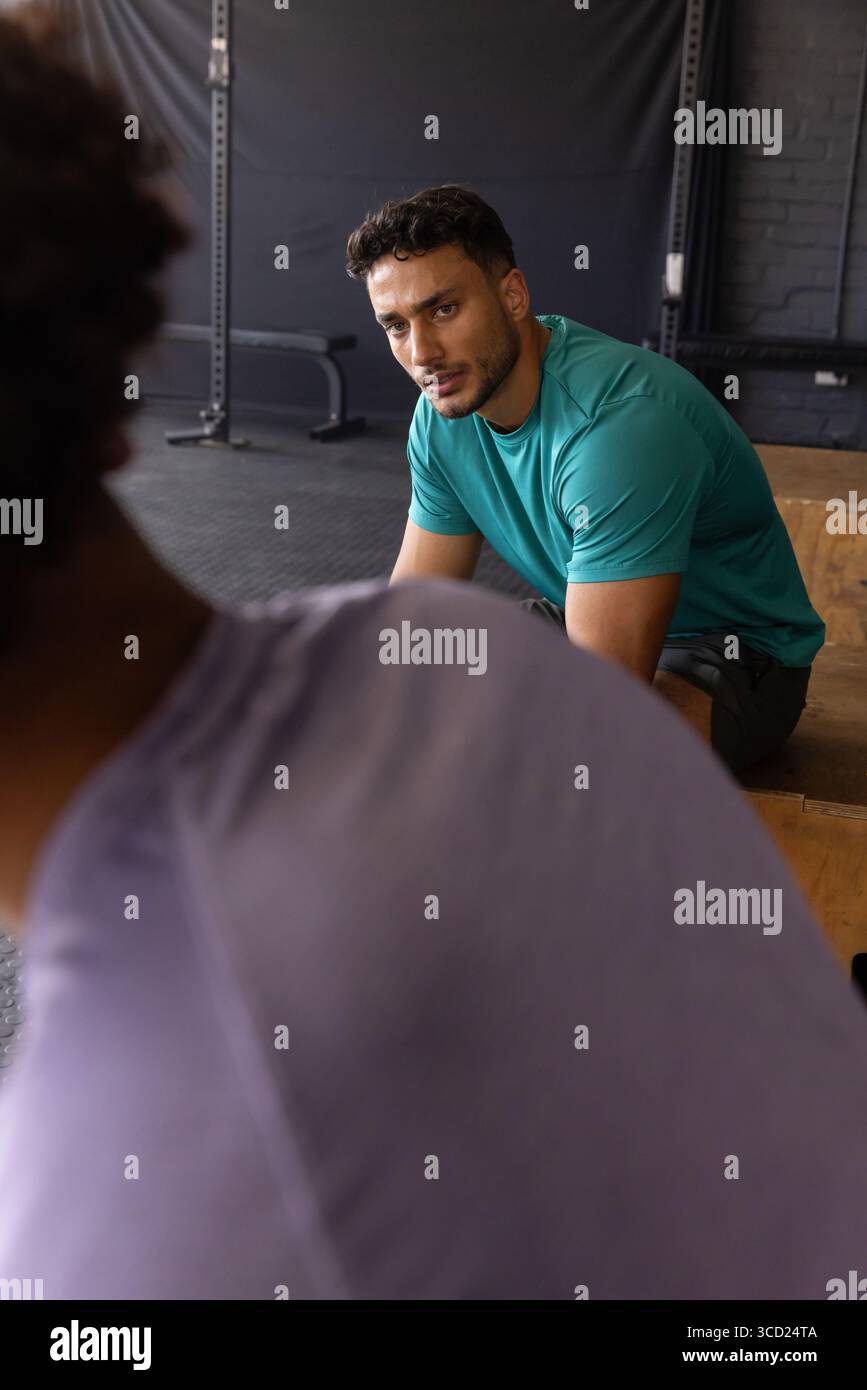 Compagni di allenamento maschili che si inclinano in avanti ascoltando i suggerimenti per l'allenamento sulla scatola plyometrica in legno in palestra Foto Stock