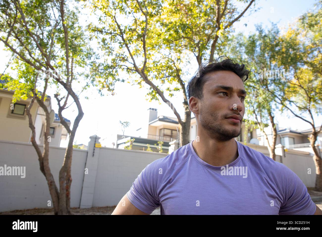 Uomo che indossa una camicia atletica viola in piedi accanto al muro che guarda direttamente sulla strada suburbana, copia lo spazio Foto Stock