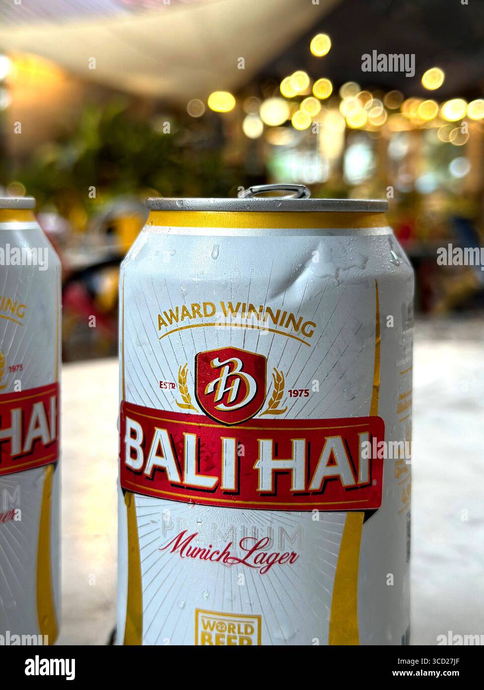 Due lattine di birra Bali hai Munich Lager su un tavolo da bar in marmo con luci bokeh sfocate sullo sfondo che creano un'atmosfera festosa, Penang, Malesia - Immagine stock catturata con smartphone