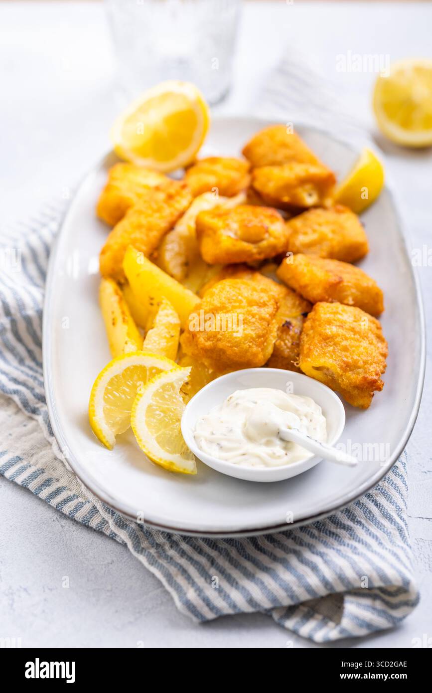 Pesce e patatine tradizionali con salsa al limone e tartaro sul piatto da portata Foto Stock