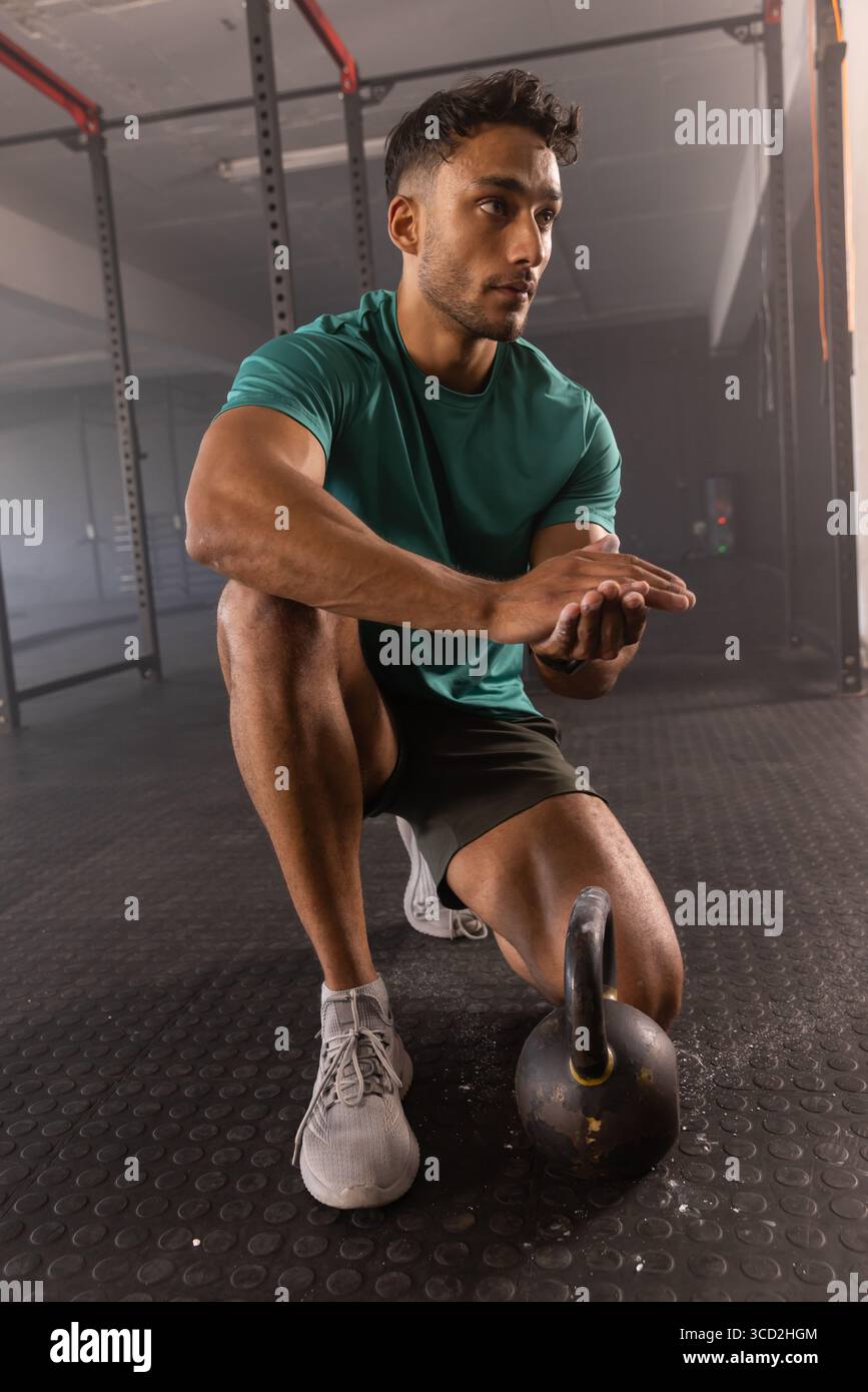 Uomo inginocchiato sul pavimento in gomma sfregando la polvere di gesso sui palmi con un campanello sotto lo scaffale in metallo Foto Stock