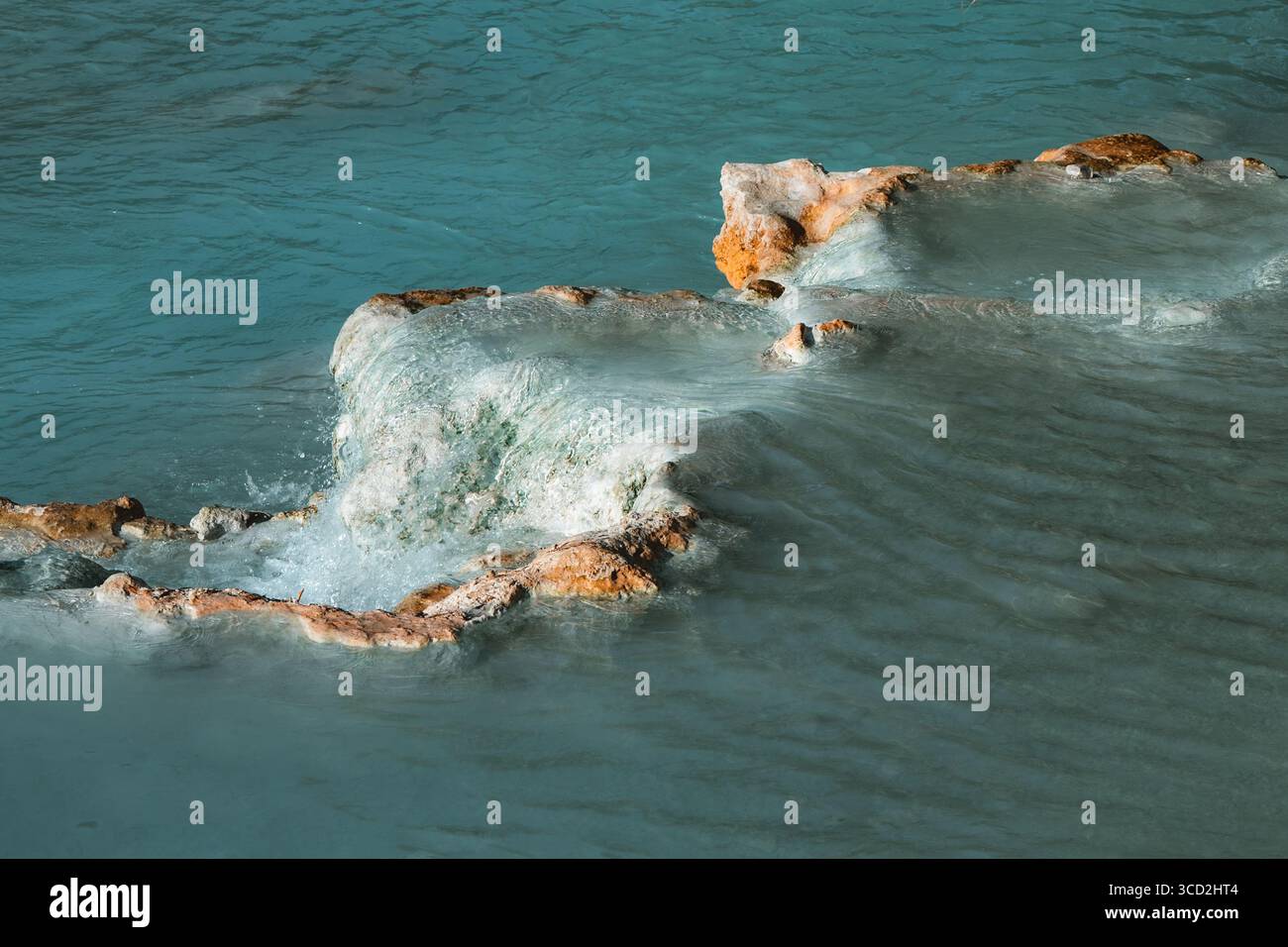 Vista delle acque turchesi che si infrangono su calde rocce terrazzate che creano un'ipnotica danza di colore e consistenza, Saturnia, Toscana, Italia. Foto Stock