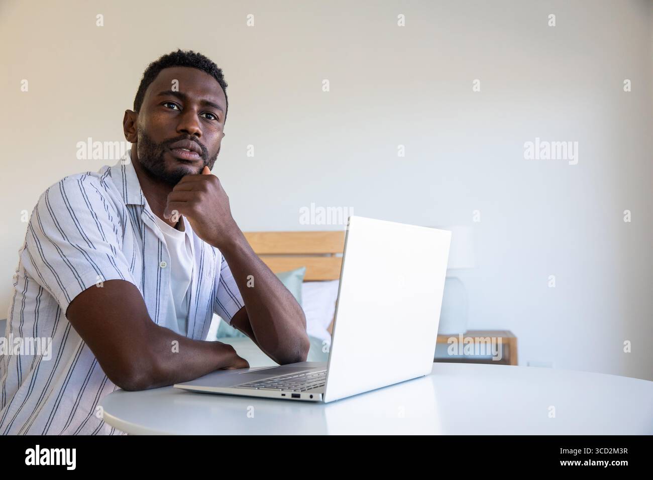 Uomo afroamericano medio adulto che lavora su un computer portatile argentato in camera da letto, spazio fotocopie Foto Stock