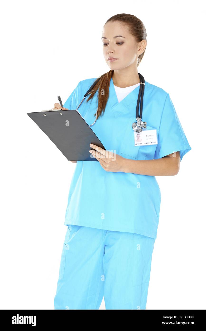 Bella giovane infermiera in scrub verdi in piedi scrivendo appunti su un appunti con un'espressione seria isolata sul bianco Foto Stock