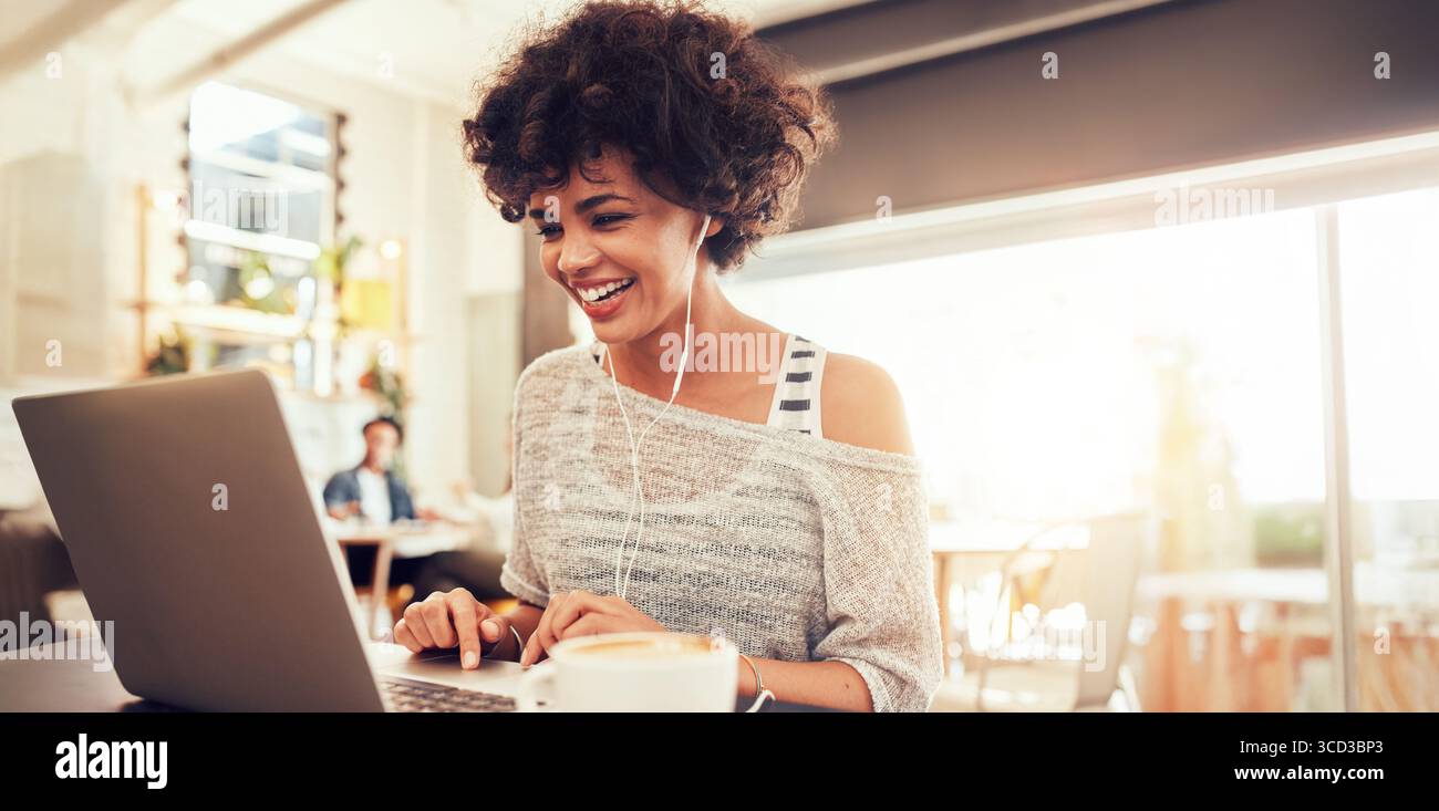 Donna che lavora su un notebook in un bar, rappresenta il lavoro da remoto, lo stile di vita freelance e la cultura nomade digitale. Concetto ideale per il lavoro online. Foto Stock