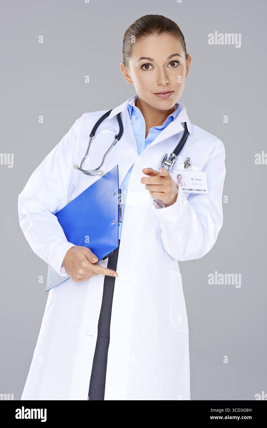 Giovane donna attraente portatore medico una lima blu in piedi che punta alla fotocamera con un'espressione seria isolata sul grigio Foto Stock