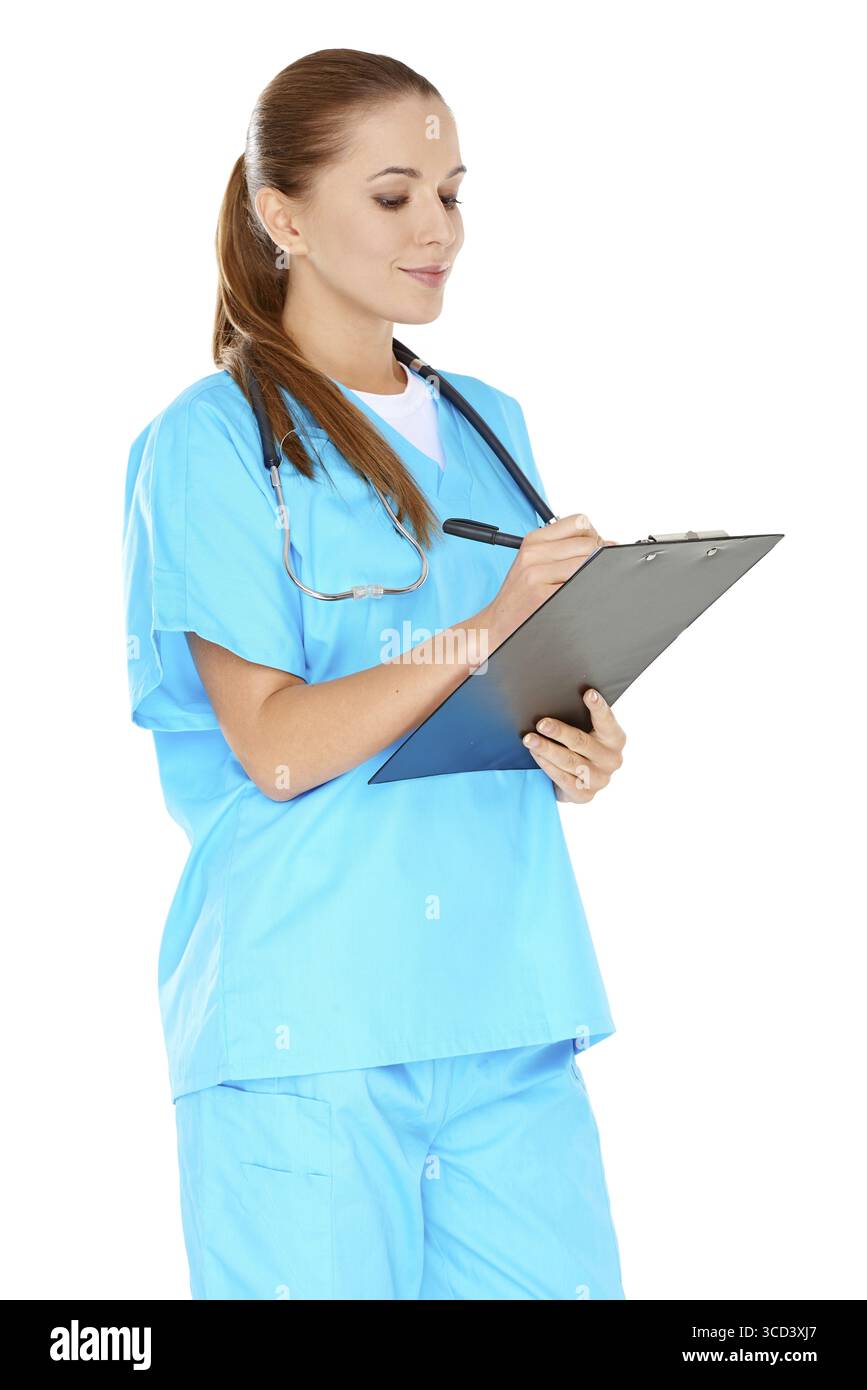 Bella giovane infermiera in scrub verdi in piedi scrivendo appunti su un appunti con un'espressione seria isolata sul bianco Foto Stock