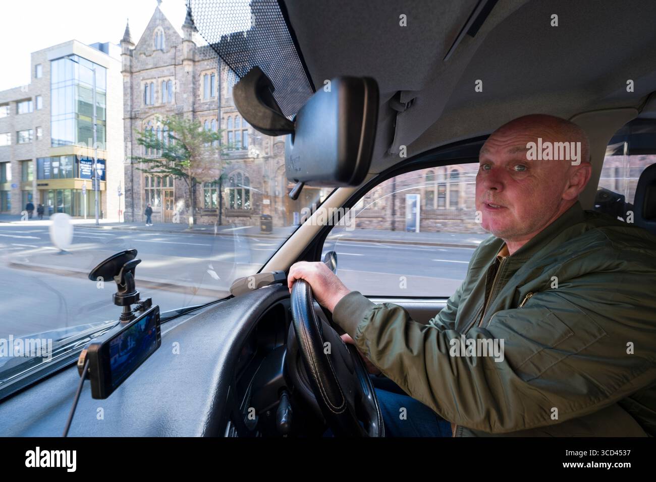Guida maschile che guida un taxi durante un tour in taxi nero di Belfast, Contea di Antrim, Irlanda del Nord, Regno Unito Foto Stock