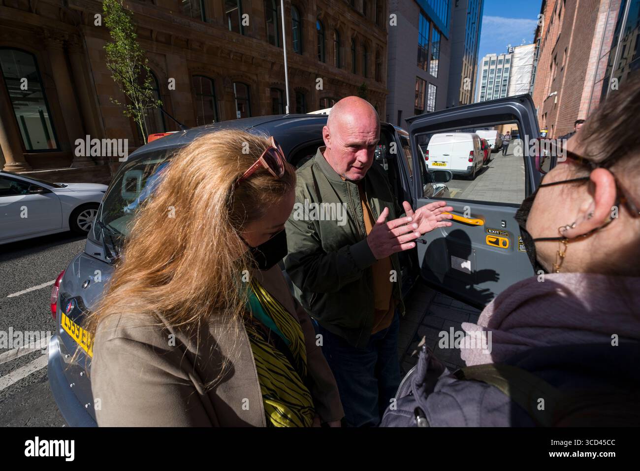 Guida maschile che parla con una turista femminile durante un tour in taxi nero di Belfast, Contea di Antrim, Irlanda del Nord, Regno Unito Foto Stock