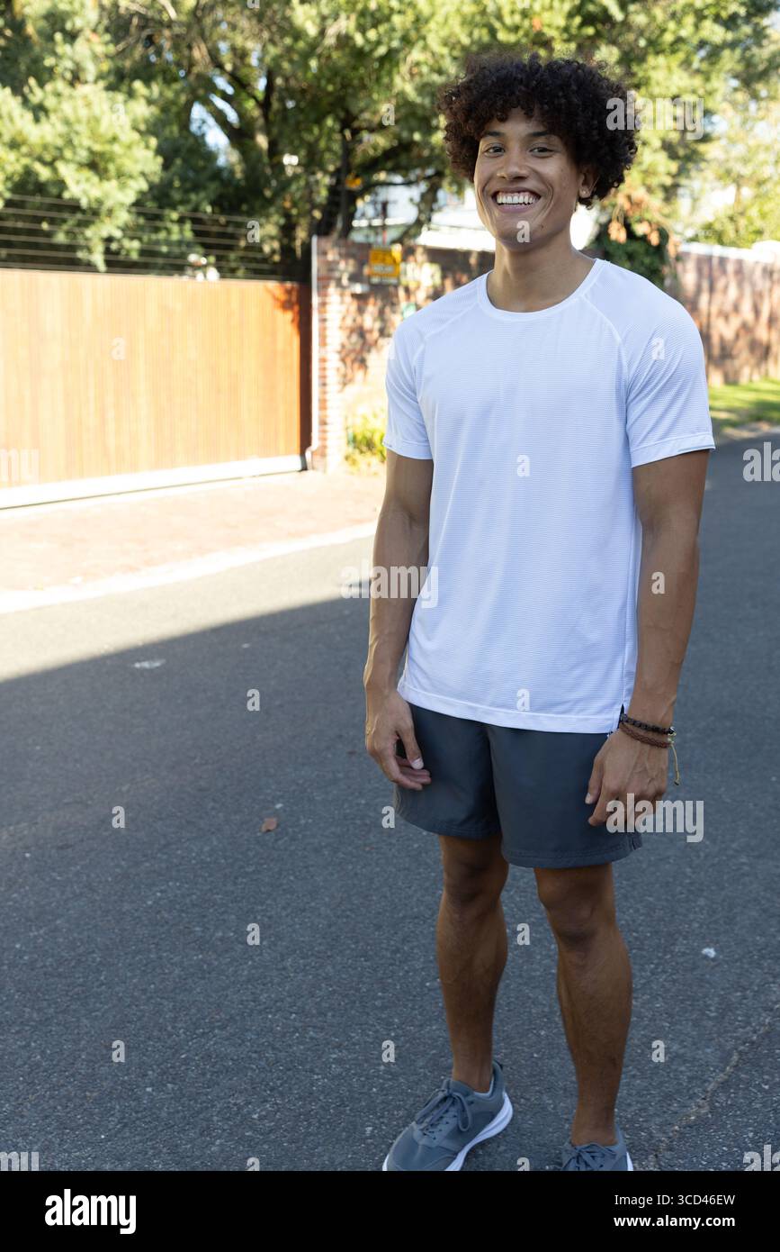 Uomo afroamericano in piedi per strada alla luce del sole, indossa abiti sportivi con braccialetti Foto Stock