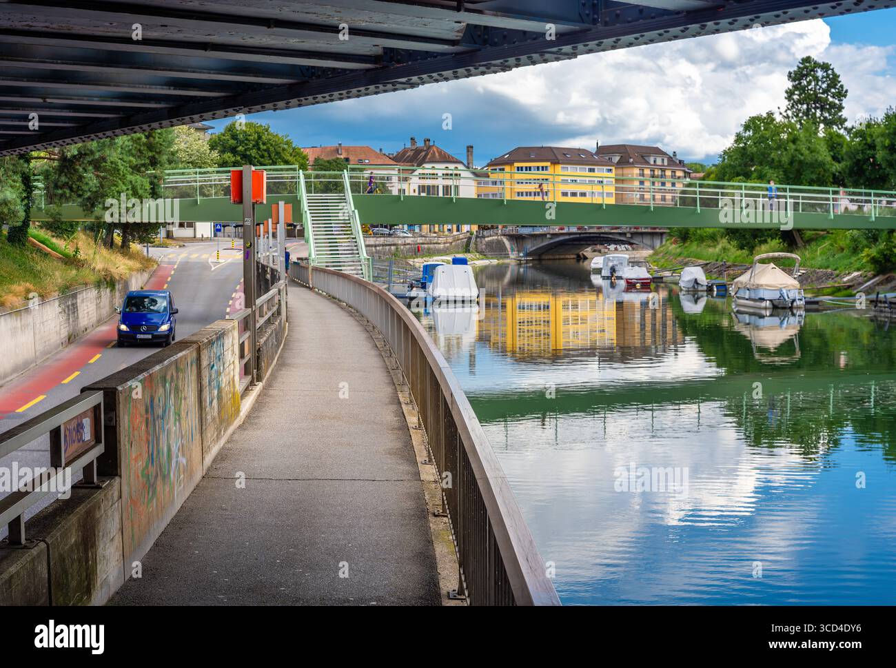 Yverdon les Bains, Svizzera - 24 luglio 2025: Vista sul canale delle barche, ponte pedonale verde e riflessi sull'acqua. L'area circostante include Foto Stock