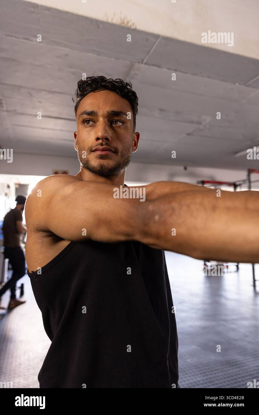 Uomo ventenne che indossa una canotta che si allunga con le braccia in avanti sui portapacchi della palestra Foto Stock Uomo ventenne che indossa una canotta che si allunga con le braccia in avanti sui portapacchi della palestra Foto Stock