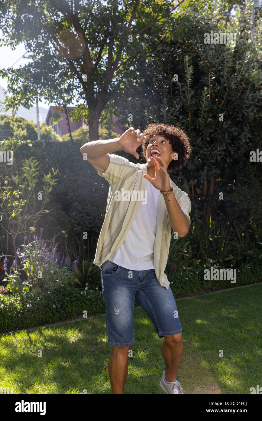 Uomo ispanico in piedi su un vivace prato in giardino sotto un albero alto, che protegge gli occhi dal sole Foto Stock