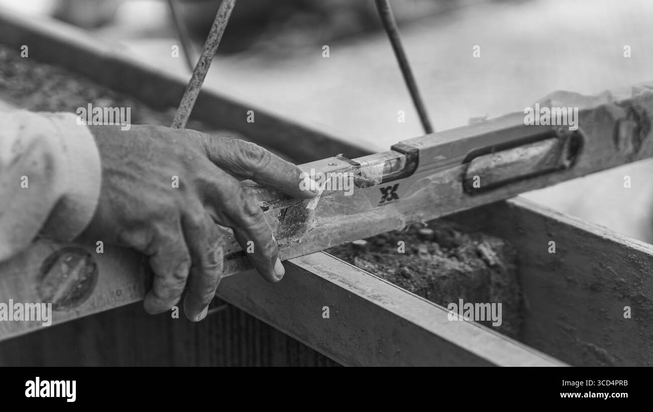 Una livella a bolla d'aria si appoggia sul calcestruzzo per garantire l'uniformità della superficie, un passo essenziale per mantenere precisione e qualità nei lavori di costruzione Foto Stock