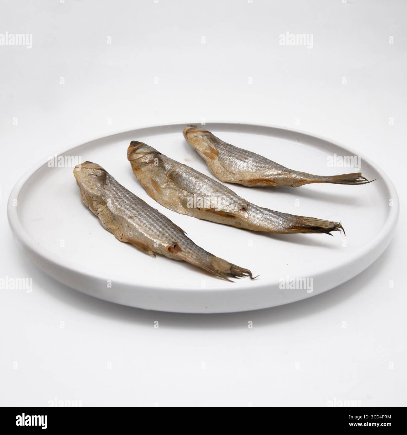 Tre pesci secchi posti su un piatto bianco. Tradizionale spuntino a base di pesce conservato, spesso servito con birra o utilizzato in cucina. Foto Stock