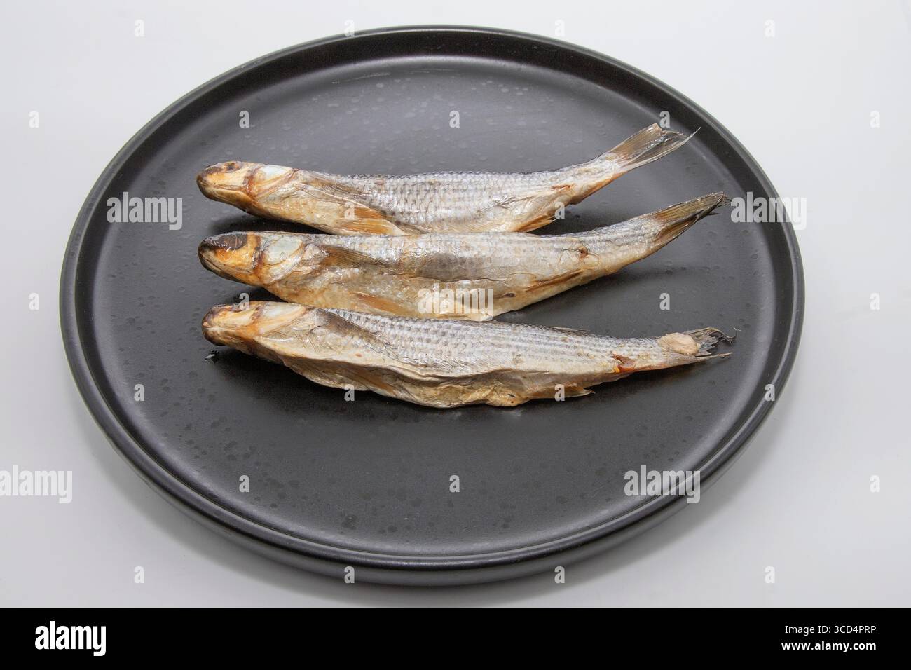 Tre pesci secchi disposti su un piatto nero. Tradizionale pesce conservato per spuntini, accompagnamento alla birra o cucina. Foto Stock
