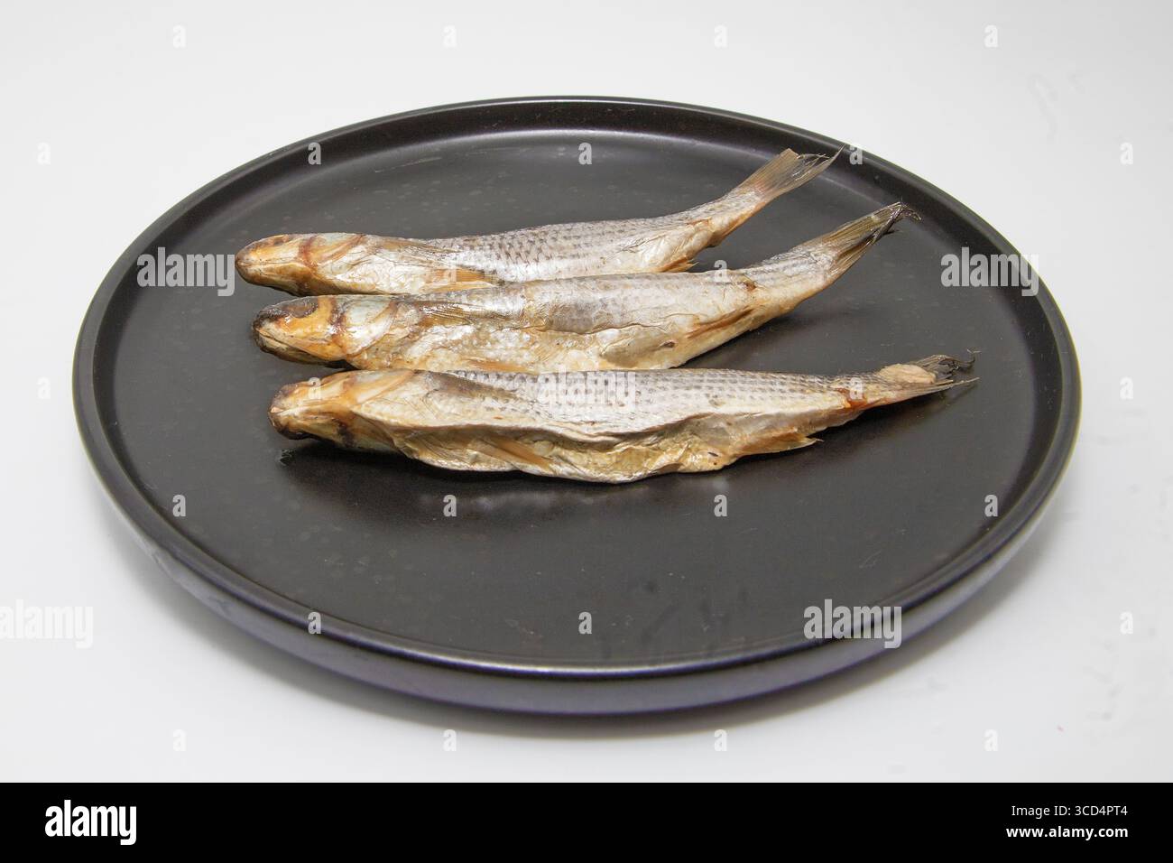 Tre pesci secchi disposti su un piatto nero. Tradizionale pesce conservato per spuntini, accompagnamento alla birra o cucina. Foto Stock