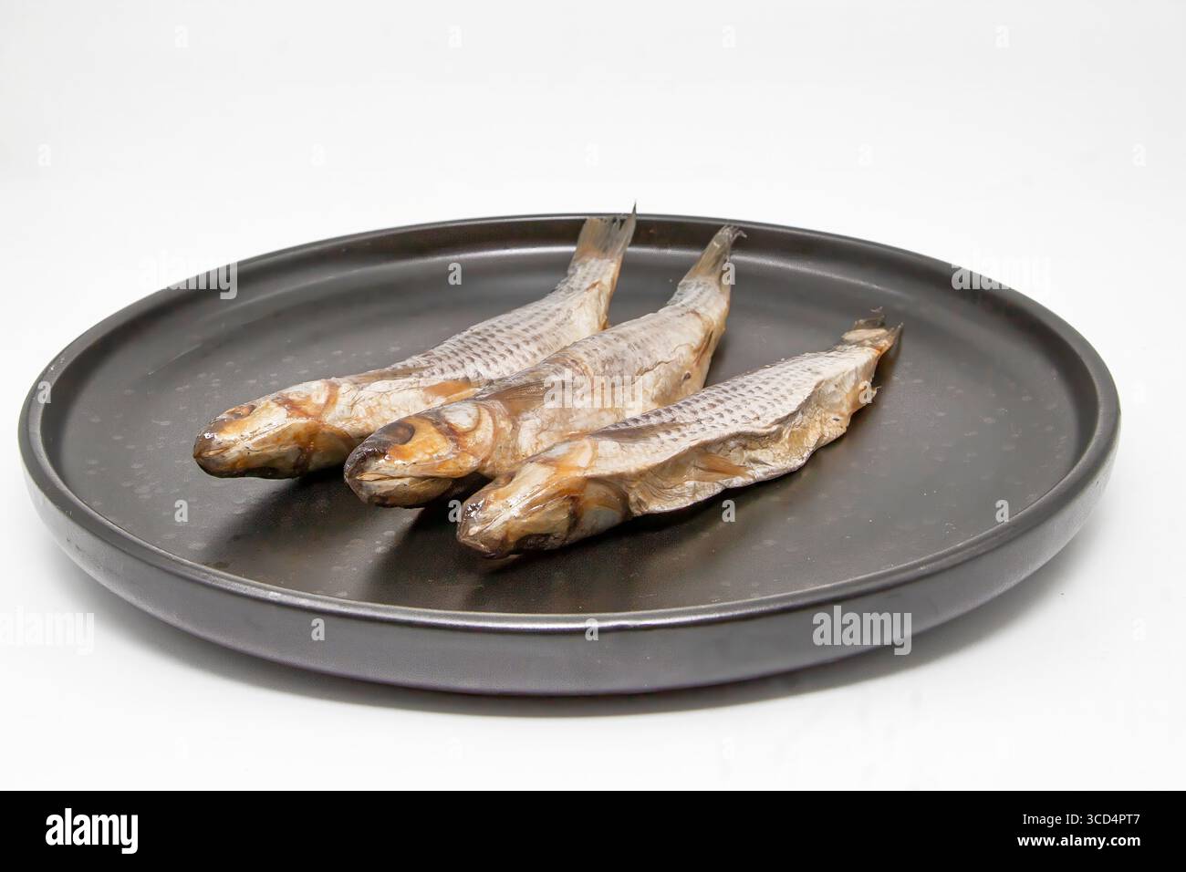 Tre pesci secchi disposti su un piatto nero. Tradizionale pesce conservato per spuntini, accompagnamento alla birra o cucina. Foto Stock