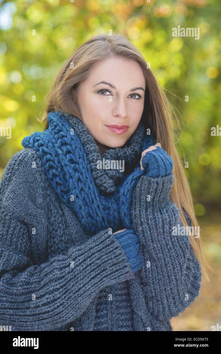 Bella giovane donna bionda con una giacca in maglia grigia spessa durante la stagione autunnale. Guardando la fotocamera. Riprese all'aperto Foto Stock
