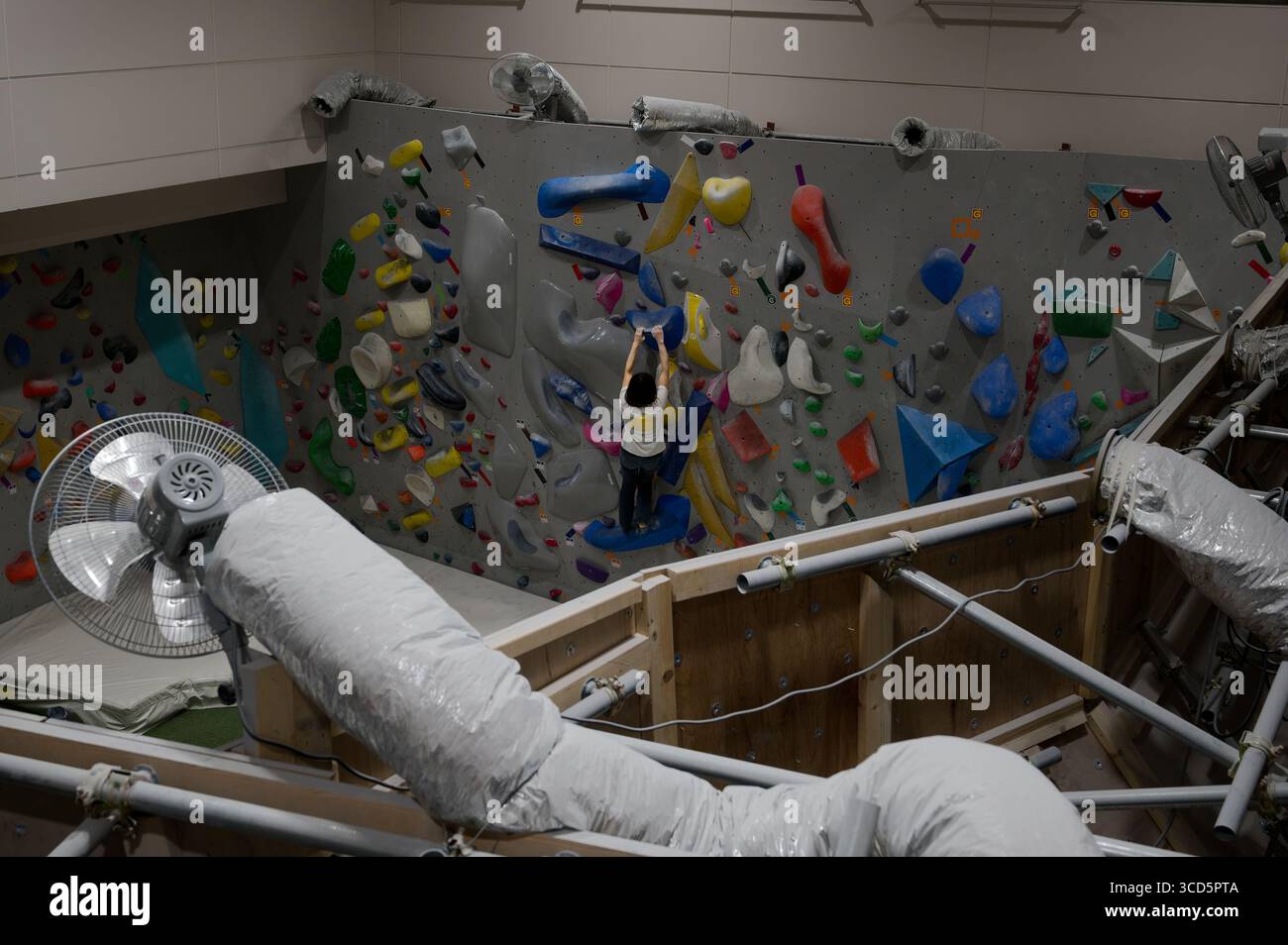 Palestra di arrampicata al coperto a Tokyo con un arrampicatore che affronta colorate massi su un percorso avanzato Foto Stock