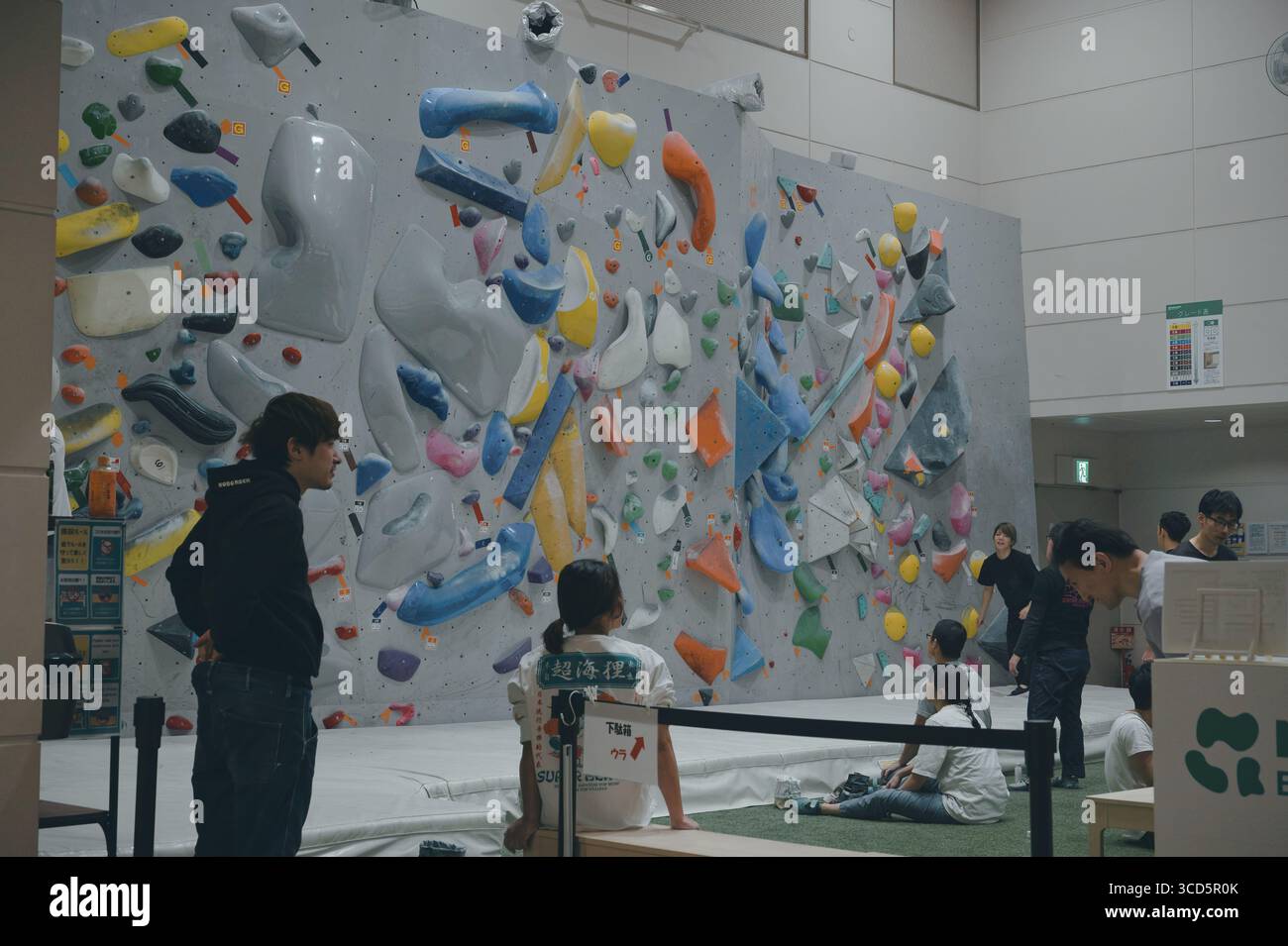 Gli scalatori si riuniscono all'interno di una palestra di bouldering di Tokyo, studiando percorsi colorati prima di salire sul muro Foto Stock