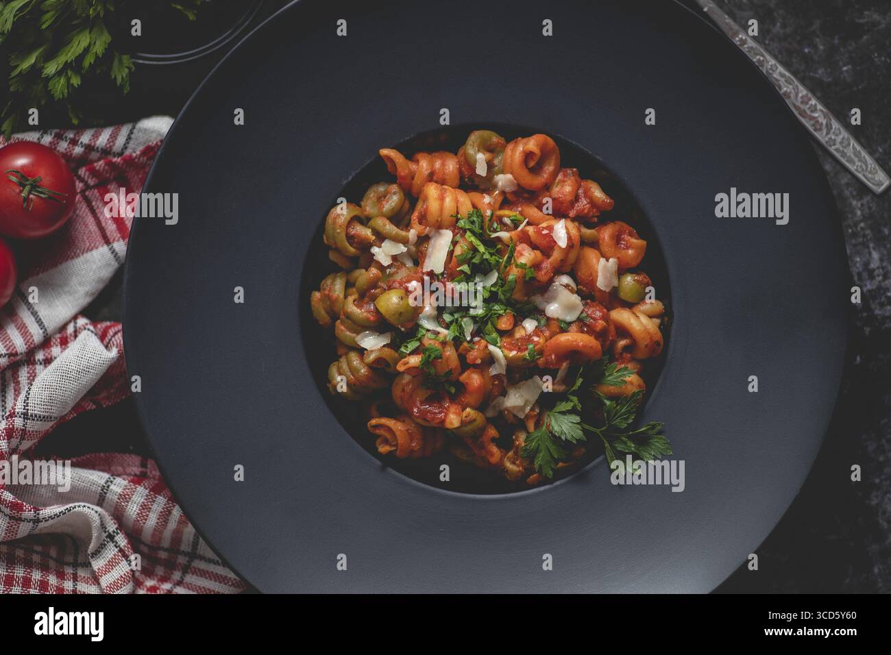 Gustosa e appetitosa pasta italiana classica con salsa di pomodoro, parmigiano e basilico su piatto al buio. Vista dall'alto piano Foto Stock