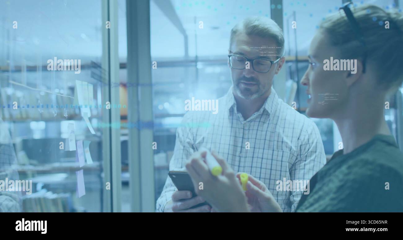 Brainstorming dei colleghi di ufficio su una parete di vetro con appunti adesivi, smartphone e pennarelli gialli Foto Stock