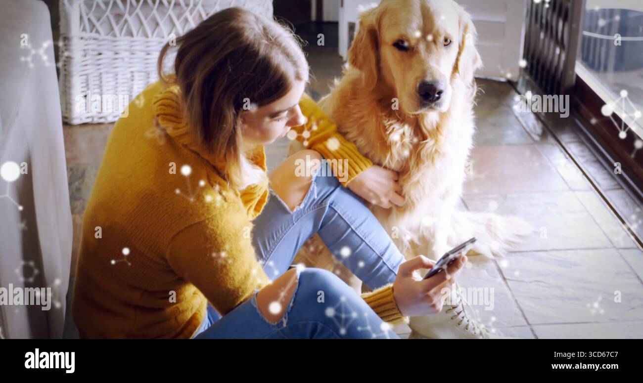 Donna pendente che indossa un maglione sul petto di vimini a casa, accarezza Golden retriever con lo smartphone Foto Stock