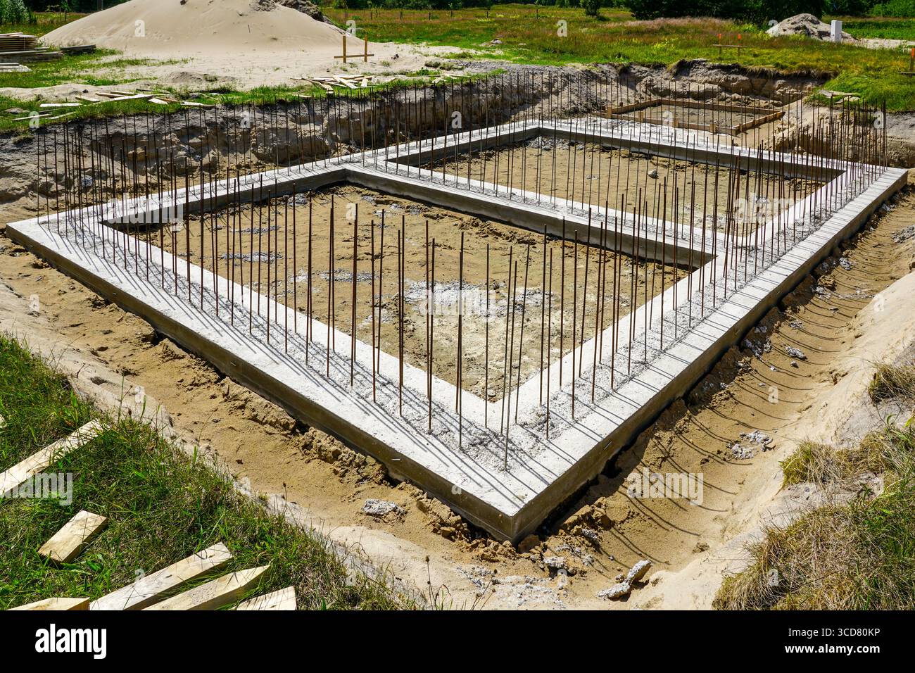 Fondazioni in calcestruzzo fresco con rinforzo verticale in armature in acciaio, che segnano la fase iniziale della costruzione di edifici residenziali o commerciali Foto Stock