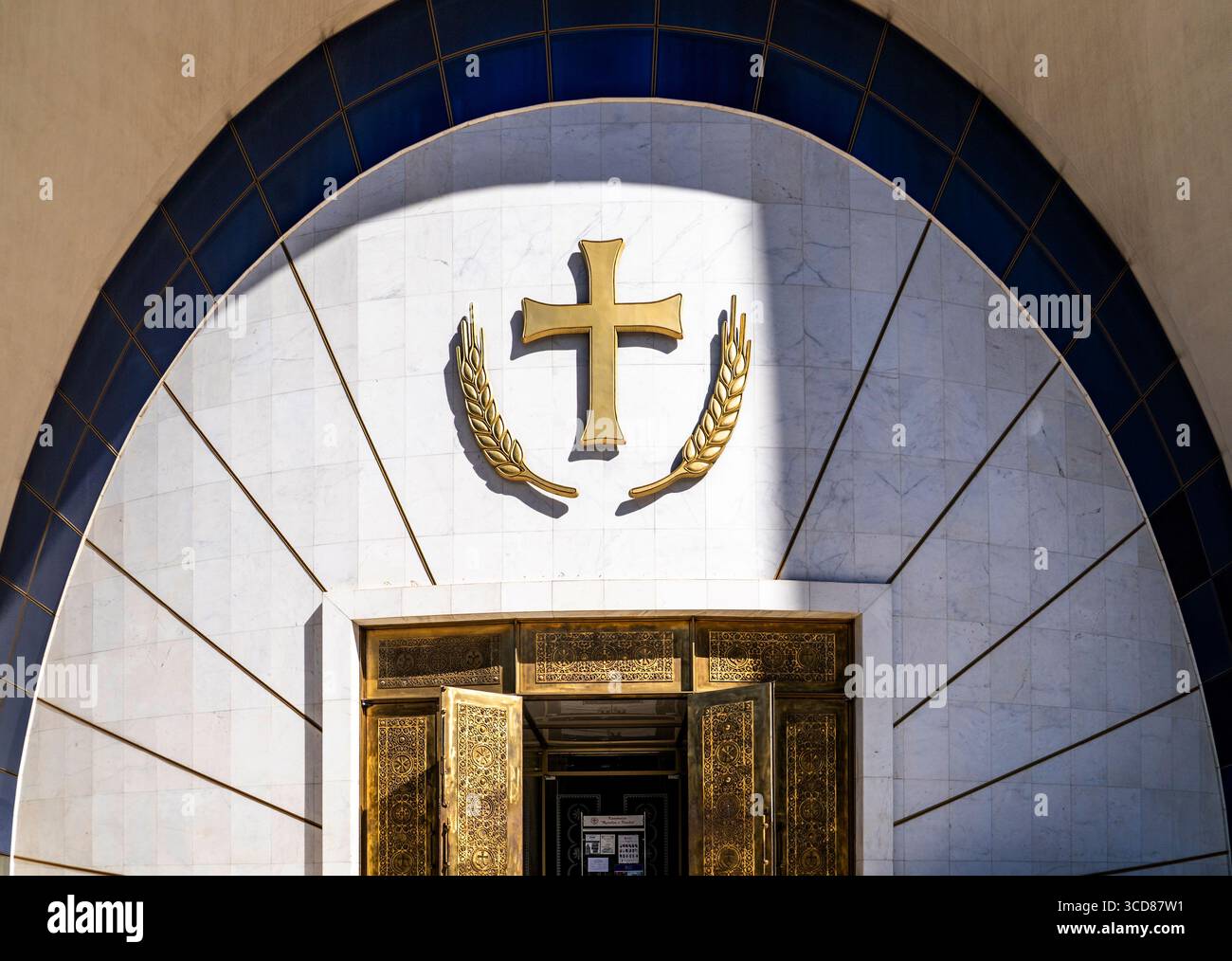 Una croce dorata e una corona d'alloro adornano un arco di marmo bianco sopra porte ornate. Foto Stock
