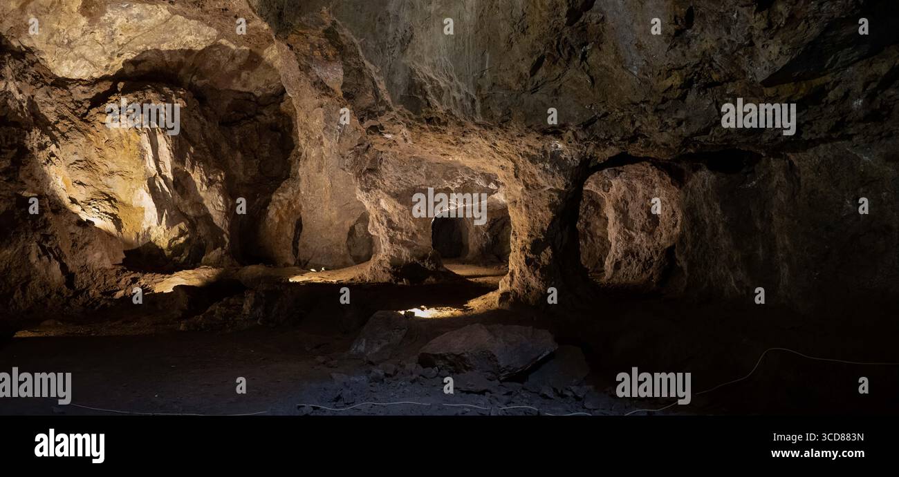 Una grotta interna poco illuminata con aspre formazioni rocciose e ombre. Foto Stock