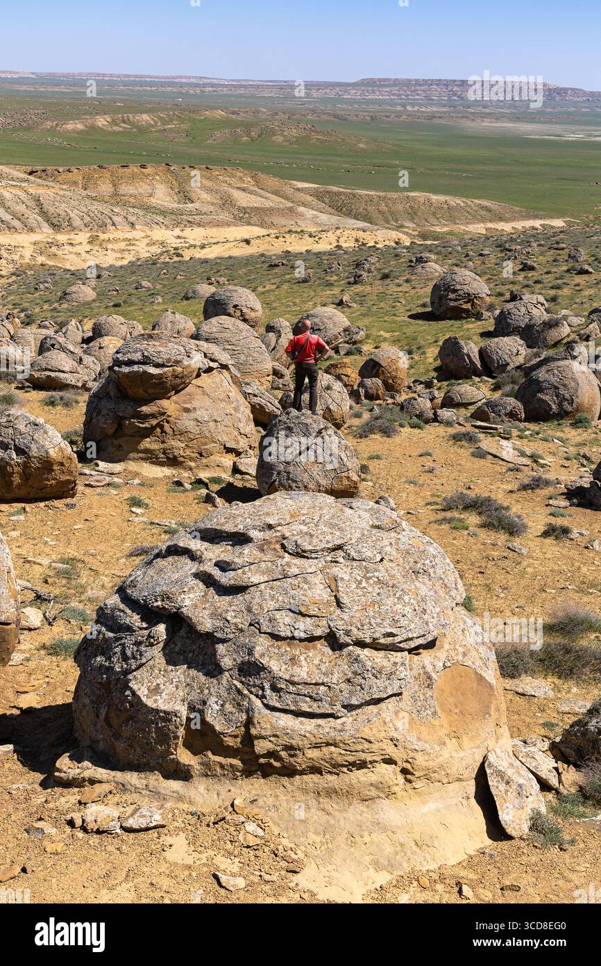 Palle di pietra nella valle Torysh con una persona non identificabile in rosso, Mangystau, Kazakistan occidentale. Concrezioni minerali di oggetti marini milioni di anni Foto Stock