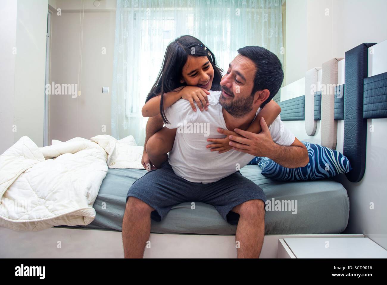 Un padre single che si è appena svegliato ride mentre sua figlia lo abbraccia Foto Stock