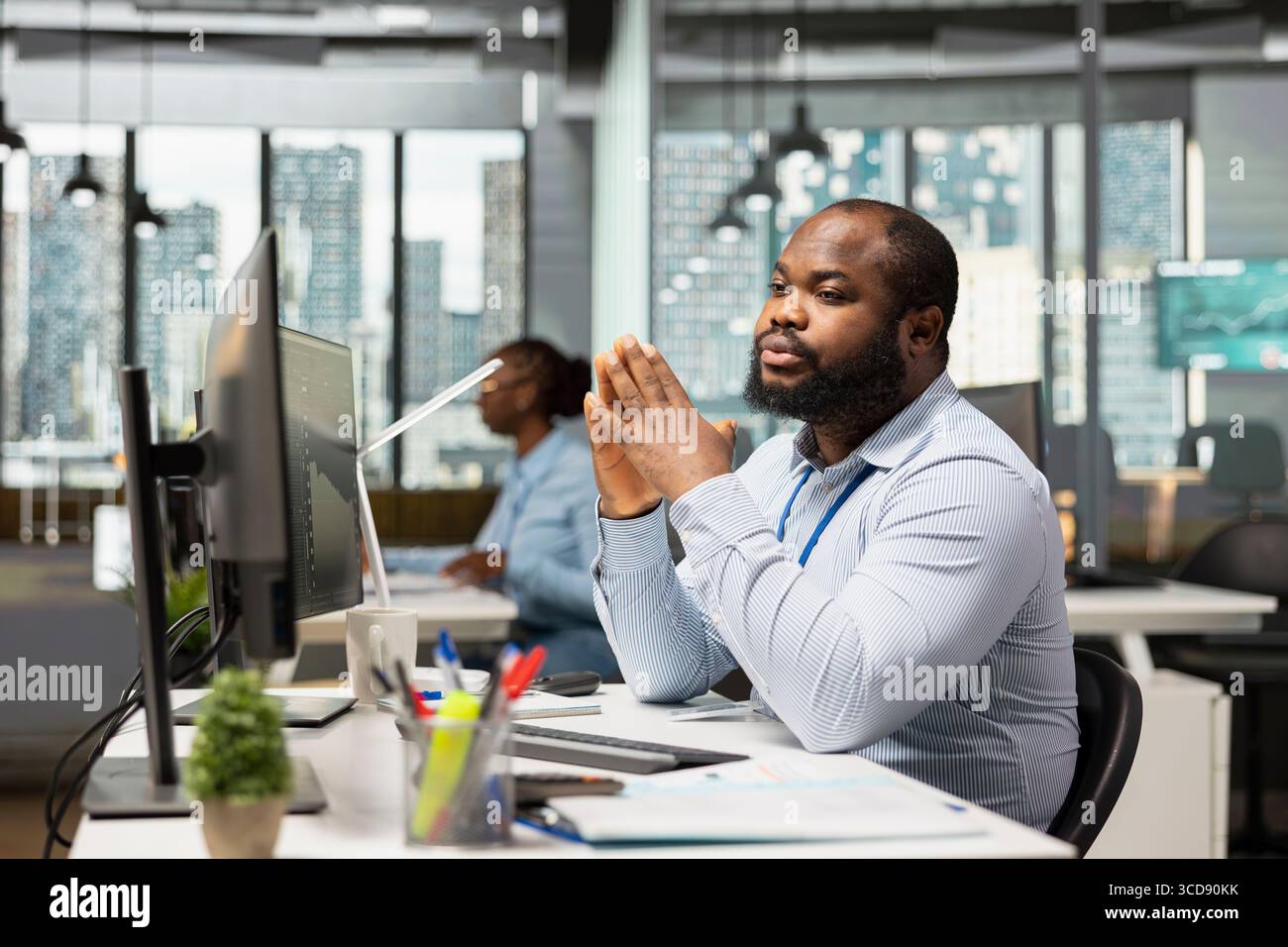 Trader in un'azienda proprietaria che monitora i prezzi di borsa su più schermi, negoziando titoli. Uomo afroamericano che utilizza software di trading per regolare le strategie di hedge durante le oscillazioni di mercato Foto Stock