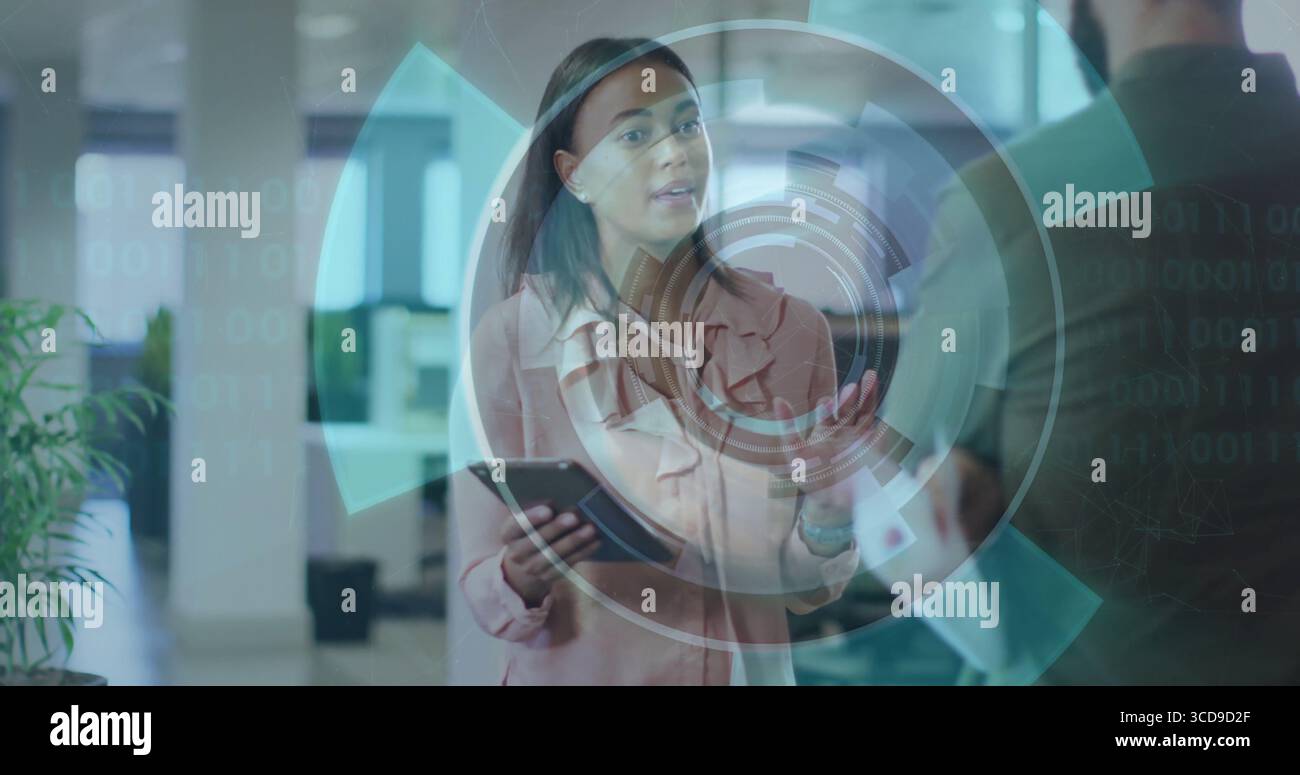 Donna in camicetta rosa che tiene in mano un tablet in ufficio, rivede un display olografico circolare Foto Stock