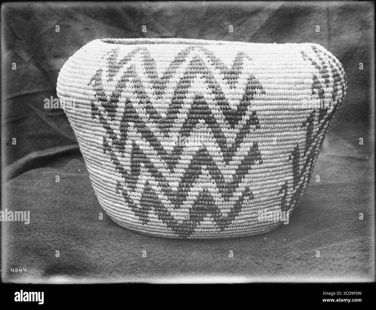 Un cestino dei nativi americani è allestito su uno sfondo di stoffa, un tradizionale oggetto artigianale risalente al 1900 circa. Foto Stock