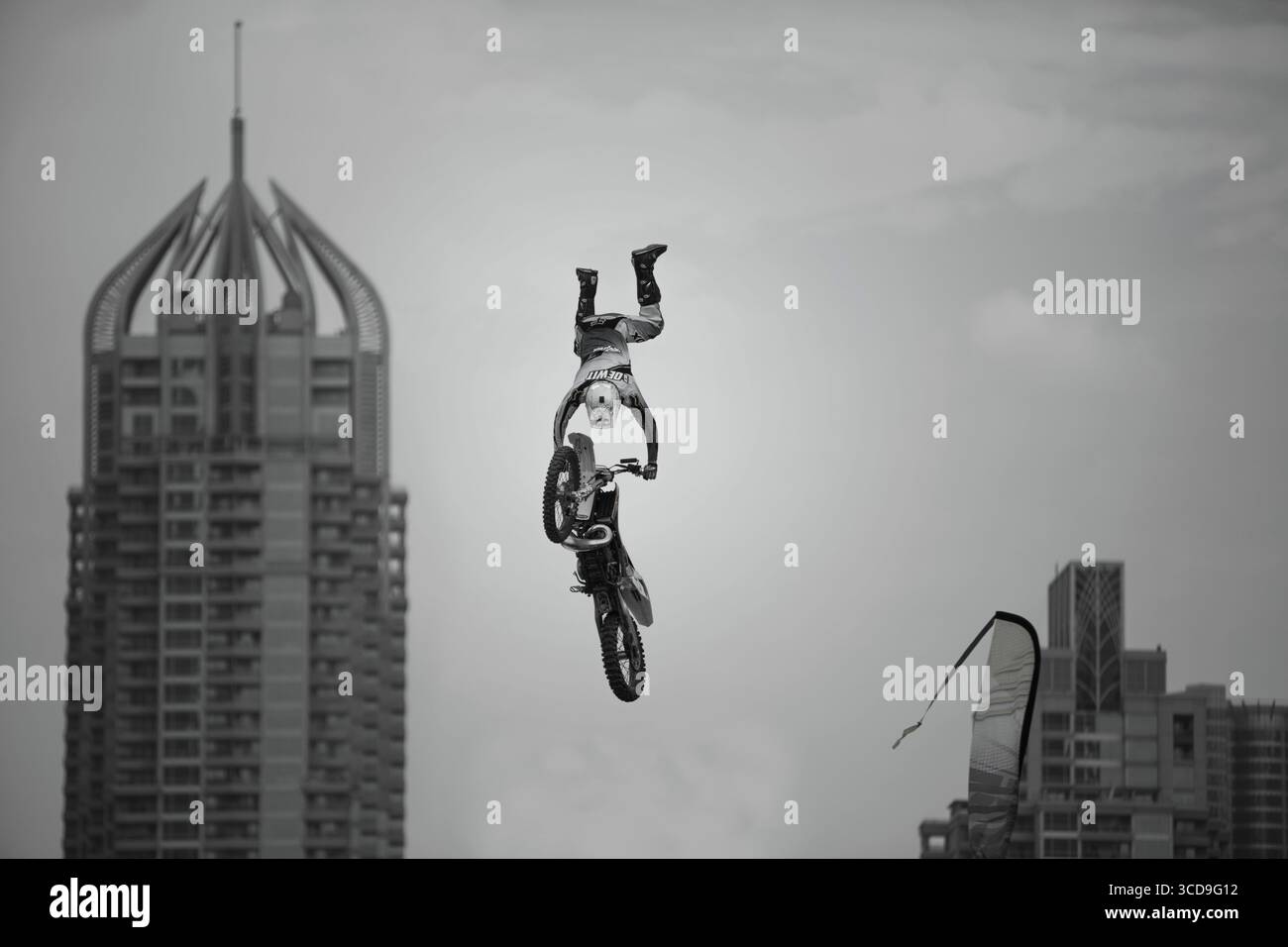 Pilota di motocross freestyle che esegue una acrobazia aerea ad alta quota sopra i grattacieli di una città moderna durante una mostra di sport estremi urbani. Foto Stock